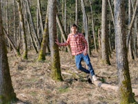 Portrait of Samuel in the woods. Leaning on a tree trunk standing in the middle of the picture, among trees.